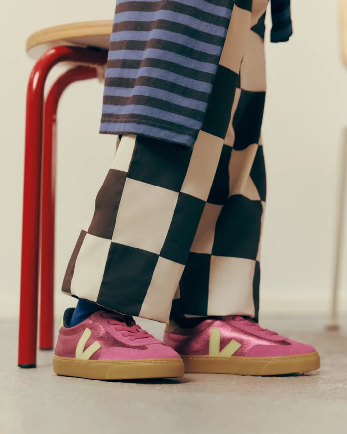 A person standing in front of a red stool wearing wide-leg checkered trousers, a striped top, and pink Veja sneakers with yellow logo accents.