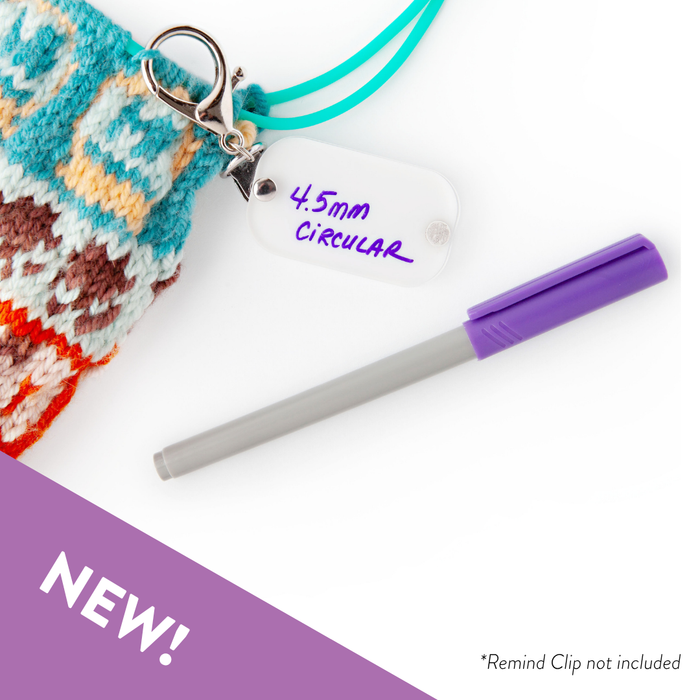 Wet erase marker shown writing needle size on a Remind Clip tag attached to colorful knitted fabric
