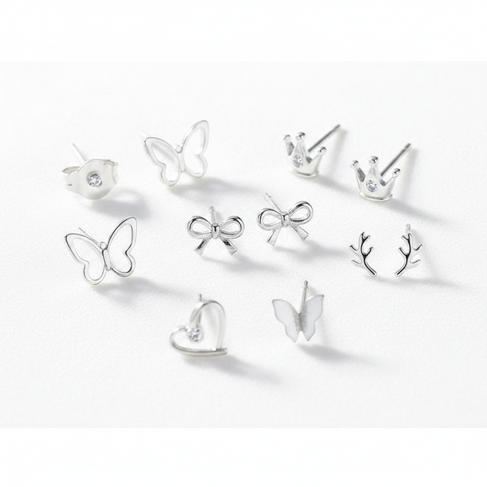 A high-resolution product shot of a collection of dainty sterling silver stud earrings in various shapes, including butterflies, crowns with small crystals, bows, antlers, and a heart, all displayed on a clean white surface.