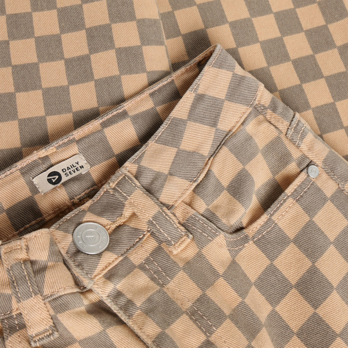Close-up of the waistband and front pocket area of a pair of pants in a beige and taupe checkerboard pattern, with a visible Daily Team label and metal button.