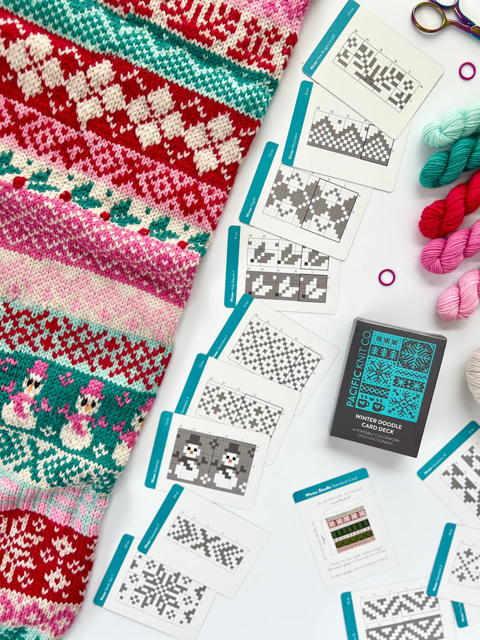 Winter Doodle chart cards fanned beside a red and green Fair Isle knit and mini skeins