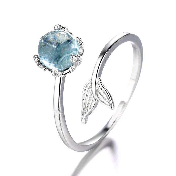 A polished sterling silver adjustable open ring featuring a round blue crystal centerpiece and a detailed mermaid tail on the opposite end, displayed on a pure white background.