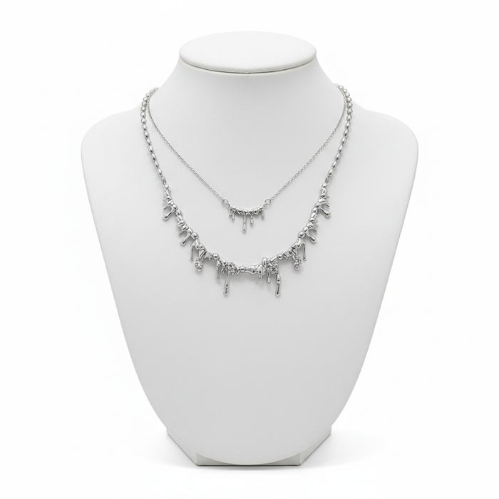 A luxury layered necklace set in silver featuring two tiers of molten dripping metal pendants on a white minimalist mannequin bust.