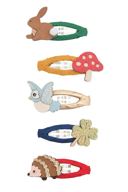 Five children's hair clips arranged vertically on a white background, each shaped like a different woodland character or object: a rabbit on green elastic, a mushroom, a bird, a four-leaf clover, and a hedgehog on red fabric.