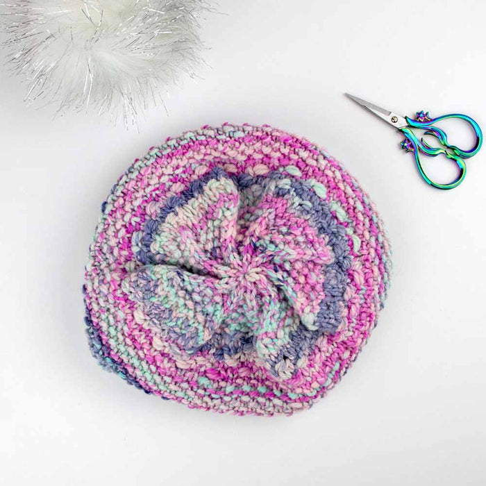 Top view of multicolor knitted Wrapped Together beanie hat showing crown decreases with scissors and pom pom