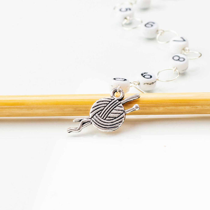 Close-up of silver yarn ball with knitting needles charm on numbered bead chain row counter resting on bamboo needle