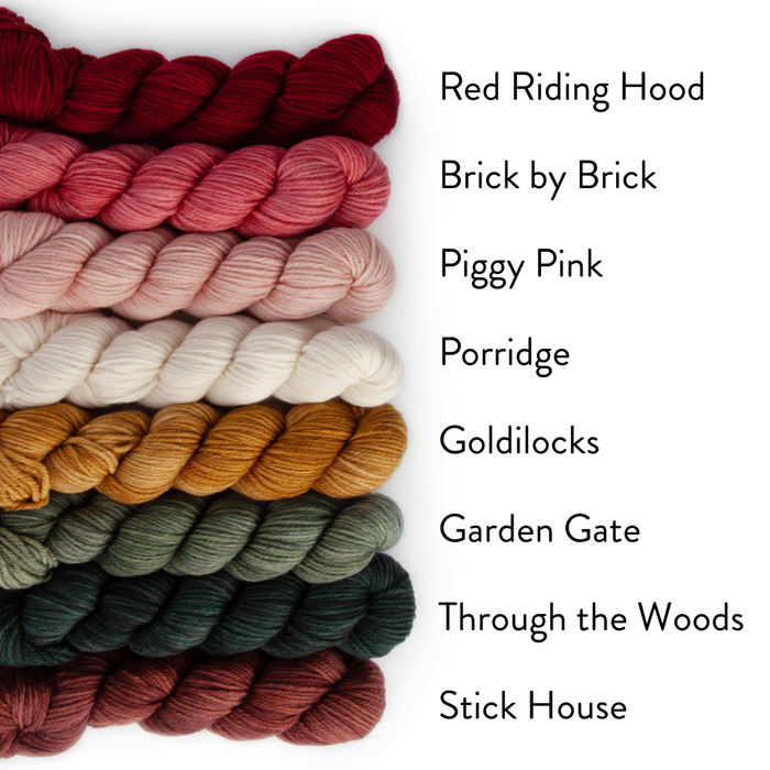 Eight mini skeins of Yarnaceous Storybook DK Doodle yarn stacked horizontally with colorway names labeled Red Riding Hood deep crimson and Brick by Brick rose pink and Piggy Pink light pink and Porridge cream white and Goldilocks golden mustard and Garden Gate sage green and Through the Woods dark teal and Stick House deep burgundy